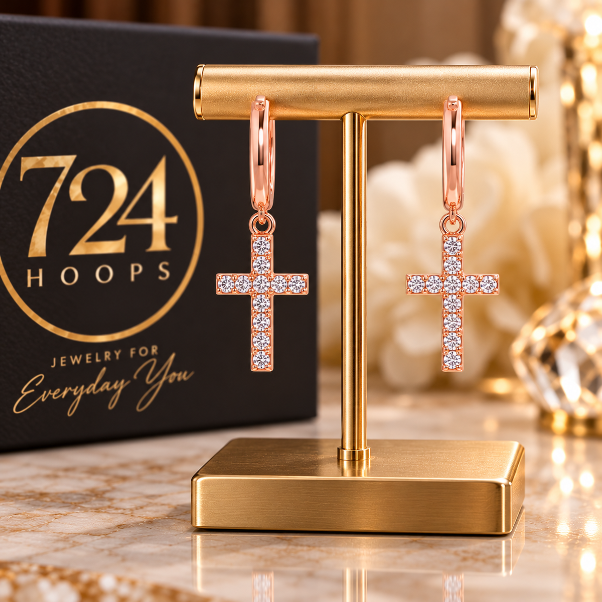 Styled promotional image of rose-gold CZ cross hoop earrings on a gold jewelry stand with 724 Hoops branding