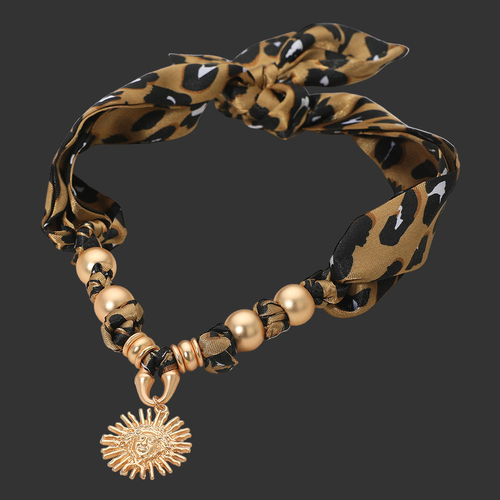 Leopard print necklace with gold beads and sun charm on a black background